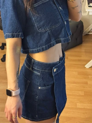 Croppad jeans set ZARA - Säljer ett supersnyggt set från ZARA bestående av en croppad skjorta i mörkblå denim i strl XS samt matchande shorts/kjol i strl S. Använt vid endast ett tillfälle och är i nyskick. 