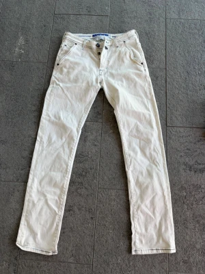 Vita jeans från Jacob Cohën - Snygga vita jeans från Jacob Cohën, tillverkade i Italien. Klassisk rak passform med blå kontrastsömmar och knappgylf. Perfekta för dig som vill sticka ut med stilrena detaljer och exklusiv känsla.