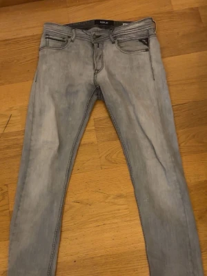 Ljusgråa skinny jeans från Replay - Säljer ett par ljusgråa skinny jeans från Replay med klassisk femficksdesign. Jeansen har en snygg tvättad look och svarta detaljer på bakfickan. Perfekta för dig som gillar en smal passform och stilren design.
