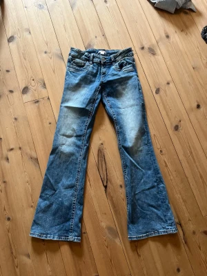 Blå bootcut jeans med låg midja - Säljer ett par blå bootcut jeans med låg midja och slitningar framtill. Jeansen har klassisk femficksmodell och är tillverkade i denim med lätt stretch. Perfekta för en avslappnad och trendig look.