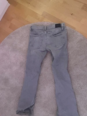 Gråa raka jeans - Snygga grå jeans med rak passform och klassisk femficksdesign. Jeansen har bälteshällor och knappgylf. Perfekta till en avslappnad stil och passar till det mesta. Materialet känns som bomull med lite stretch.