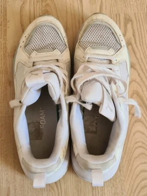 Vita sneakers från Puma - Säljer ett par vita sneakers från Puma med meshdetaljer på tån och sidorna för extra ventilation. Skorna har klassisk snörning, tjock sula och diskret Puma-logga på plösen. Materialet är en mix av textil och syntet, vilket ger en sportig och fräsch look.