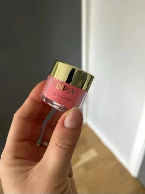 DIPSY Dip Powder röd nagelpulver - DIPSY Dip Powder i en snygg röd nyans, perfekt för att skapa trendiga och hållbara naglar. Kommer i en liten burk med guldfärgat lock. Pulvret ger en jämn och intensiv färg till dina naglar och är lätt att applicerat.