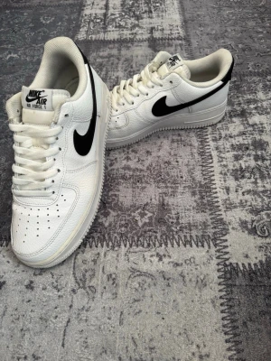 Nike Air Force 1 vita sneakers - Klassiska Nike Air Force 1 sneakers i vitt skinn med svart swoosh på sidan. Lågt skaft, perforerad tåbox för ventilation och Tidlös design som passar till det mesta och ger en. Pris kan diskuteras 