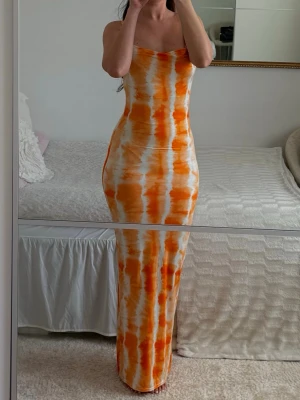 Orangevit långklänning - Orange/vit maxiklänning i tie dye-mönster. Väldigt smickrande och figurnära passform som sitter superfint på kroppen. Perfekt till semester, strandmiddag, beach club eller sommarkvällar. Stretchigt och bekvämt material