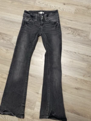 Svarta bootcut jeans med slitningar - Snygga svarta bootcut jeans med lätt slitna detaljer och klassisk femficksdesign. Jeansen har normalhög midja och subtila tvättade partier framtill för en cool look. Perfekta för dig som gillar en avslappnad men trendig stil.