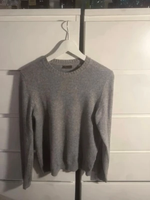 Ljusgrå kashmir tröja Stenströms - Ljusgrå kashmir tröja från Stenströms med rund halsringning och ribbade muddar. Tröjan har en klassisk och stilren design, perfekt för lager-på-lager och passar till många olika outfits. Materialet ser ut att vara mjukt och bekvämt.