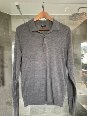 Grå långärmad pikétröja Uniqlo - Snygg grå långärmad pikétröja från Uniqlo i tunn, mjuk ullmix. Tröjan har klassisk krage, knäppning med tre knappar och ribbade muddar vid ärmslut och nederkant. Storleken är Small, inga defekter på tröjan utan den är i mycket bra skick. Hör av dig vid några funderingar!