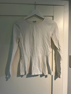 Vit långärmad topp med utsvängd midja - Snygg vit långärmad topp med rund halsringning och lätt utsvängd nederdel. Tillverkad i mjuk bomull, perfekt för en clean och enkel look. Passar dig som gillar stilrena basplagg med en twist.