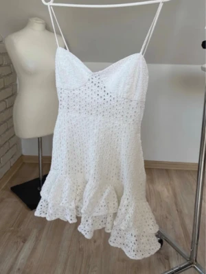  Ny trendig Vit kort klänning med volang - Söt vit kort klänning med smala axelband och volangkant nertill. Klänningen är ärmlös och har ett broderat spetsmönster som ger en romantisk känsla. Perfekt för varma dagar och somriga tillfällen.