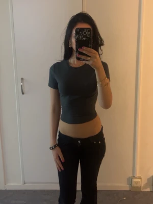 Mörkgrå croppad topp - Snygg mörkgrå croppad topp med korta ärmar och rund hals. Tight passform som framhäver midjan, perfekt till höga jeans eller kjol. Enkel och stilren design utan mönster eller detaljer.