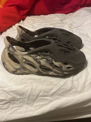 Yeezy Foam Runner sandaler grå/beige - Unika Yeezy Foam Runner sandaler i grå och beige med marmorerat mönster. Tillverkade i lätt och flexibel EVA-foam med futuristisk design och många ventilationshål för maximal komfort. Perfekta för dig som vill sticka ut med en modern och trendig look.