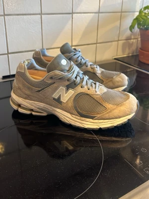 New balance skor  - Stilrena grå New Balance 2002r sneakers med mesh och mockadetaljer. Ikoniskt N på sidan, chunky vit sula och klassisk siluett. Perfekta för dig som gillar streetwear och sportig vibe.
