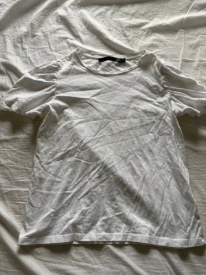 Vit puffärmad t-shirt från Lager 157 - Säljer en vit t-shirt från Lager 157 med puffärmar och rund hals. T-shirten är gjord i mjuk bomull och har en klassisk passform med korta ärmar som ger en söt och trendig look. Perfekt till jeans eller kjol för en enkel men snygg outfit.