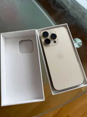 iPhone 14 Pro guld - Skriv för mer info. Snygg iPhone 14 Pro 128gb  i guld med elegant glasbaksida och rostfria kanter. Telefonen har tre stora kameralinser och Apples klassiska logga på baksidan. Kommer i originalkartong. Perfekt för dig som vill ha en modern och kraftfull smartphone.