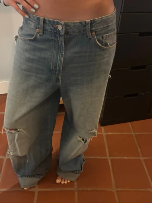 Baggy slitna blå jeans - Säljer ett par ljusblå baggy jeans med bred passform och slitningar på båda benen. Köpta på Zara och är i st 38. 