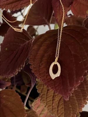 Vattentålig, Guldhalsband 925 sterling silver. Hypoallergenic  - Snyggt halsband i guld med ett ovalt, asymmetriskt hänge täckt av små gnistrande stenar. Kedjan är tunn och elegant, perfekt för att ge en extra touch till din outfit. Hänget har en modern design som sticker ut.
