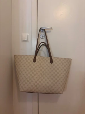 H&M tote bag i beige/brunt 🤎 - Säljer denna rymliga och stilrena väska från H&M. Perfekt till skolan, jobbet eller vardagen då den rymmer mycket. Använd men i fint skick. Beige mönstrad design med bruna handtag som passar till det mesta.