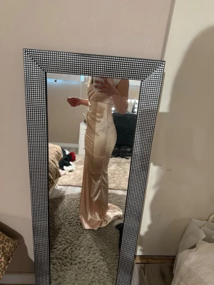 Champagnefärgad långklänning i satin - Elegant långklänning i skimrande champagnefärgad satin med figurnära passform och en öppning i ena benet. Klänningen har smala axelband och en draperad detalj vid sidan. Obs: kommer från shein, använd 1 gång på min bal i 9:an, sytt på den själv (syns inte). Säljs pga: använder aldrig 