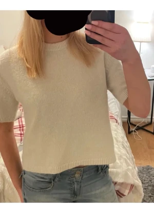Kortärmad stickad offwhite tröja - Säljer en enkel och stilren stickad tröja i offwhite med korta ärmar och rund hals. Tröjan har rak passform och ribbade kanter vid ärmslut och nederkant. Perfekt att matcha med jeans för en avslappnad look.