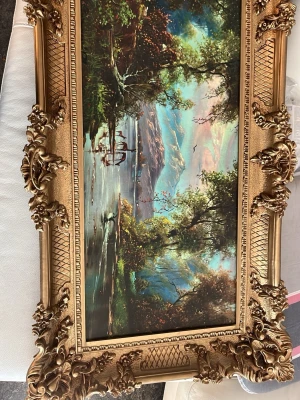 Oljemålning med guldig ram - Säljer en rektangulär oljemålning med naturmotiv som visar berg, sjö och träd i starka färger. Tavlan har en stor, detaljerad och ornamenterad ram i guld som ger en klassisk och pampig känsla. Perfekt som dekoration till vardagsrummet eller hallen.