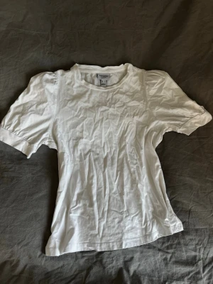 Vit puffärm t-shirt från Vero Moda - Säljer en vit t-shirt från AWARE by Vero Moda med puffärmar och rund hals. T-shirten är i mjuk bomull och har en enkel, clean look som passar till allt. Perfekt basplagg för dig som gillar stilrena outfits.