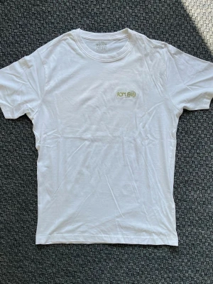 Handbroderad vit t-shirt från Denim Project - Vit T-shirt med handbroderad text ”Rom 8:18”. "Jag hävdar att den här tidens lidanden väger lätt i jämförelse med den härlighet som kommer att uppenbaras och bli vår."