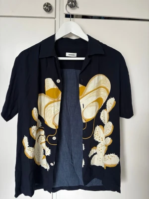  kortärmad skjorta Sandro - Unik mörkblå kortärmad skjorta från Sandro med stort tryck av cowboyhatt och kaktusar. Unik Sandro skjorta nypris 2300kr - knappt använd! Atorlek L men passar bättre som M