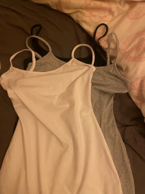 3-pack linne klänningar i svart, grå och vit - Säljer ett set med tre linne toppar i svart, grått och vitt. Alla har smala axelband och enkel, stilren design. Perfekta att matcha med olika outfits och superbekväma att bära till vardags. Materialet känns mjukt och stretchigt.