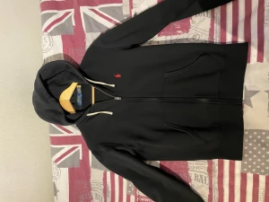 Svart hoodie från Polo Ralph Lauren - Säljer en svart hoodie från Polo Ralph Lauren med dragkedja, två fickor fram och vit dragsko i huvan. Klassisk röd logga broderad på bröstet. Tillverkad i mjuk bomull för skön känsla och stilren look. Nästintill oanvänd i storlek XS. 