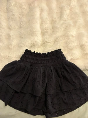 Två volangskorts i svart och blommigt - Säljer två skorts med volanger och hög smockad midja. Ena är svart med broderade hål och den andra är vit med blått småblommigt mönster. Båda har en luftig och flowy känsla, perfekta för sommaren. Materialet känns lätt och bekvämt. Säljer båda för 150 men en för 99