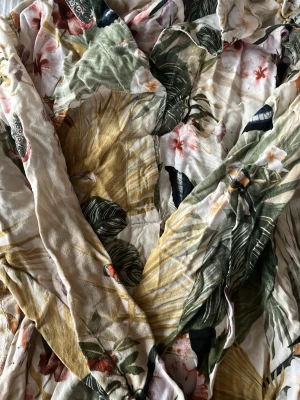 Blommig skjorta  med tropiskt mönster - Skjorta  i mjukt tyg med tropiskt blommönster i grönt, gult, rosa och vitt. Har knytskärp i midjan och avslappnad passform. Perfekt för strand dagar! Storlek 38, behöver strykas🥰