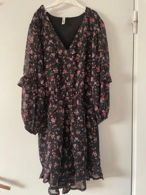 Svart blommig klänning - Svart klänning från H&M med blommigt mönster i rosa och rött. Klänningen har v-ringning, långa puffiga ärmar med volangdetaljer och ett snöre i midjan. Klänningen har shorts under!!💞