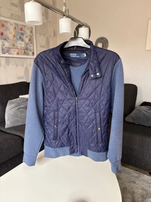 Marinblå Polo Ralph Lauren cardigan - Snygg marinblå overshirt från Polo Ralph Lauren med quiltat mönster på fram- och baksida samt mjuka blå ärmar. Jackan har ståkrage, dragkedja och tryckknappar vid fickorna. Perfekt för lager-på-lager och en stilren look.