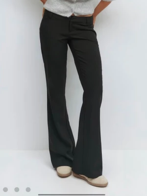 Svarta utsvängda kostymbyxor - Snygga svarta kostymbyxor med utsvängda ben och pressveck. Byxorna har fickor både fram och bak samt hällor för skärp. Perfekta för en stilren look och passar till många olika outfits.