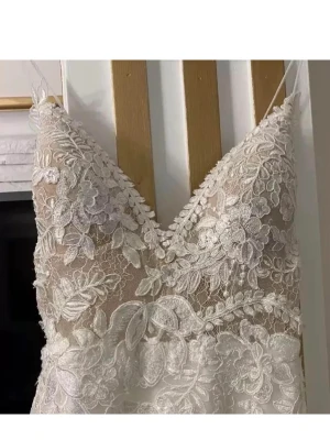 Brudklänning - Drömmig vit brudklänning från milla nova, inköpt för 20.000kr med djup v-ringning och tunna axelband. Klänningen har vackra broderade spetsdetaljer och blommigt mönster över hela tyget. Perfekt för dig som vill ha en romantisk och elegant look. Säljes billigt då jag verkligen vill bli av med den