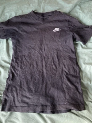 Svart Nike t-shirt - Klassisk svart t-shirt från Nike med vit logga på bröstet. T-shirten har rund halsringning och korta ärmar. Tillverkad i mjuk bomull för en skön känsla och enkel stil.