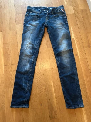 Blå slim fit jeans från Replay - Snygga blå slim fit jeans från Replay med klassisk femficksmodell och slitna detaljer. Jeansen har normal midja, dragkedja och knappstängning samt coola kontrastsömmar. Perfekta för dig som gillar en trendig och avslappnad stil.