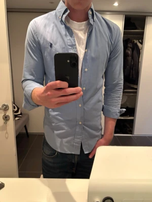 Ralph Lauren skjorta - Säljer en ljusblå ralph lauren skjorta som endast använts ett fåtal gånger, nästan nyskick. Storleken är xs men den är ganska stor i storleken så sitter som s. Om något undras över så hör gärna av dig🤩