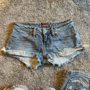 Blå lågmidjade jeansshorts från Big Star - Säljer ett par klassiska blå jeansshorts från Big Star med råa, fransiga kanter och femficksmodell. Shortsen har låg midja och slitna detaljer för en avslappnad look. Perfekta till sommaren! Passar xs/s