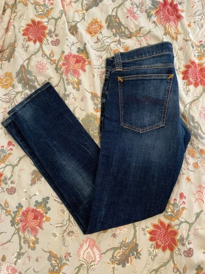 Mörkblå slim fit jeans - Säljer ett par riktigt feta mörkblåa Nudie Jeans med en skön tvätt. Dem är i väldigt bra skick och har knappt används och är tvättade max 5 gånger.                    Längd: 102 cm.                                                                           Midja: 41 cm