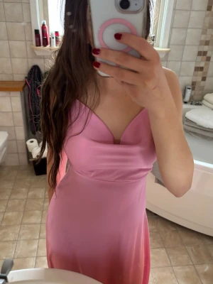 Rosa långklänning i satin-look till nians bal - Säljer en snygg rosa långklänning med mjuk satin-look och cowlneck-ringning. Klänningen har tunna axelband. Perfekt för nians bal, bröllopsgäst eller aftonklänning. Endast använd 1 gång under nians bal! Dubbeltyg vid brösten💕Jag är 165 cm och på mig går den ned till anklarna!