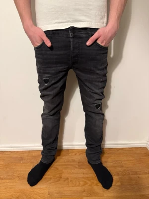 Svarta slimfit jeans med slitningar från jack&jones - Säljer ett par svarta slimfit jeans med slitningar på båda knäna och lätt tvättad look. Jeansen har klassisk femficksmodell och bra passform som sitter slim hela vägen ner. Jeansen är i storlek w30 l34. Perfekta för en trendig och avslappnad stil. Pris kan diskuteras ✅
