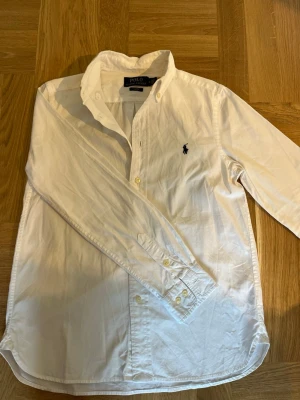 Vit skjorta från Polo Ralph Lauren - En riktigt fin vit skjorta från polo Ralph lauren. Den är endast använd ett fåtal gånger och är i ett väldigt bra skick. Köpt ny för ca 1000 kr. Den är storlek 14 i Ralph laurens ungdomsstorlekar men sitter som en xs. Priset är ej hugget i sten och skriv gärna vid funderingar! 
