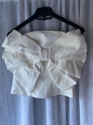 Axelbandslös topp med rosett - Supersnygg axelbandslös topp i vit färg med en rosett framme, använd fåtal gånger☺️