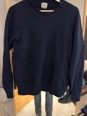 Mörkblå stickad tröja från Zara - Mörkblå stickad tröja från Zara med rund halsringning och långa ärmar. Tröjan har en enkel, stilren design och ribbade muddar vid hals, ärmslut och nederkant.