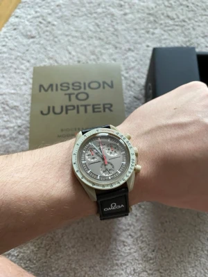 Omega x Swatch Mission to Jupiter - Säljer en Omega x Swatch Mission to Jupiter från Bioceramic MoonSwatch-kollektionen. Klockan har en beige boett, grå urtavla med flera subdials och orange sekundvisare. Svart band med Omega-logga. Kommer i originalbox med Mission to Jupiter-förpackning.