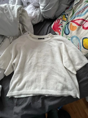 Vit stickad tröja från 157 - Säljer en enkel och stilren vit stickad tröja från 157. Tröjan har korta ärmar, rund halsringning och är gjord i ett mjukt stickat material. Perfekt för lager på lager och passar till det mesta i garderoben.