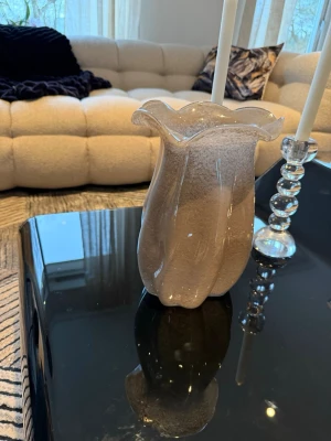 Beige vågig glasvas - Säljer en beige glasvas med vågig kant och mjuka former. Vasen har en unik design med organiska linjer och är tillverkad i glas. Perfekt som inredningsdetalj för att ge rummet en modern touch.Gjord av Lene Bjerre