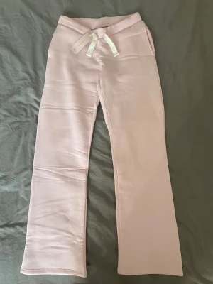 Ljusrosa mjukisbyxor med raka ben - Säljer ett par ljusrosa mjukisbyxor med raka ben och vita snören i midjan. Byxorna har två bakfickor och är gjorda i ett mjukt, skönt material som passar perfekt för chill dagar. Supersnygga att matcha med en hoodie eller crop top.